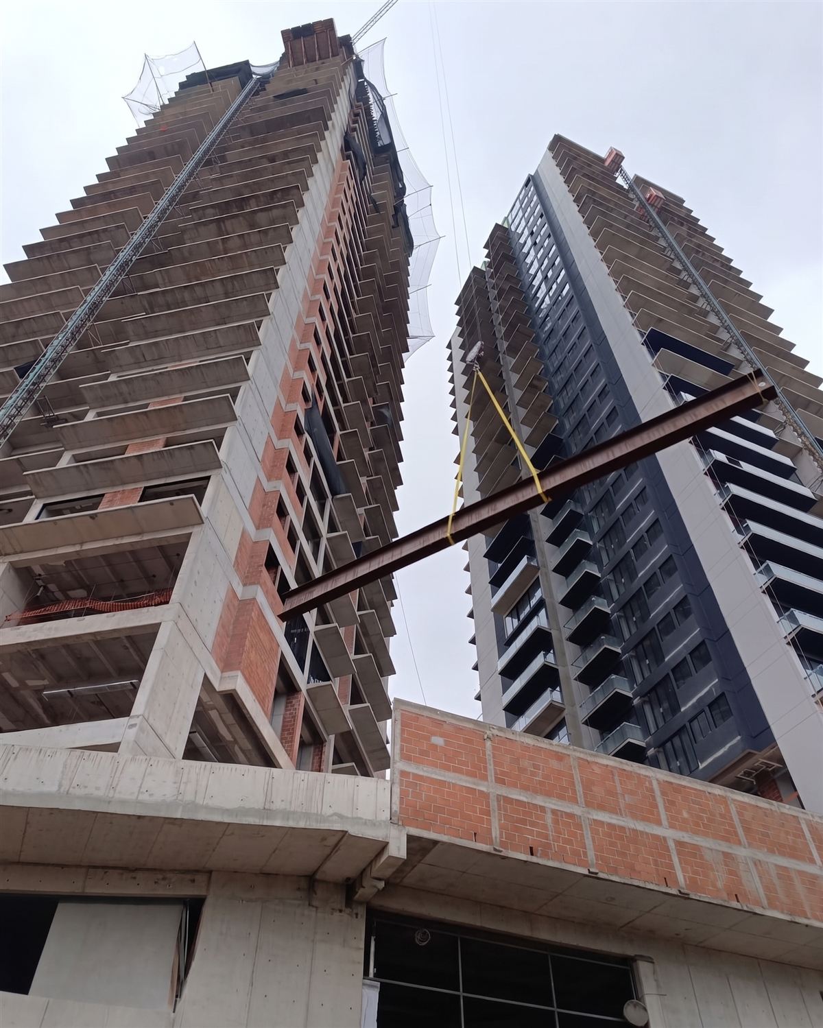 Vista desde abajo de dos torres en construcción con estructura de concreto y acero